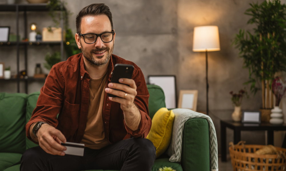 man sitting on couch smiling while on his phone to help show "what is ncua insurance" from Alliance Catholic Credit Union